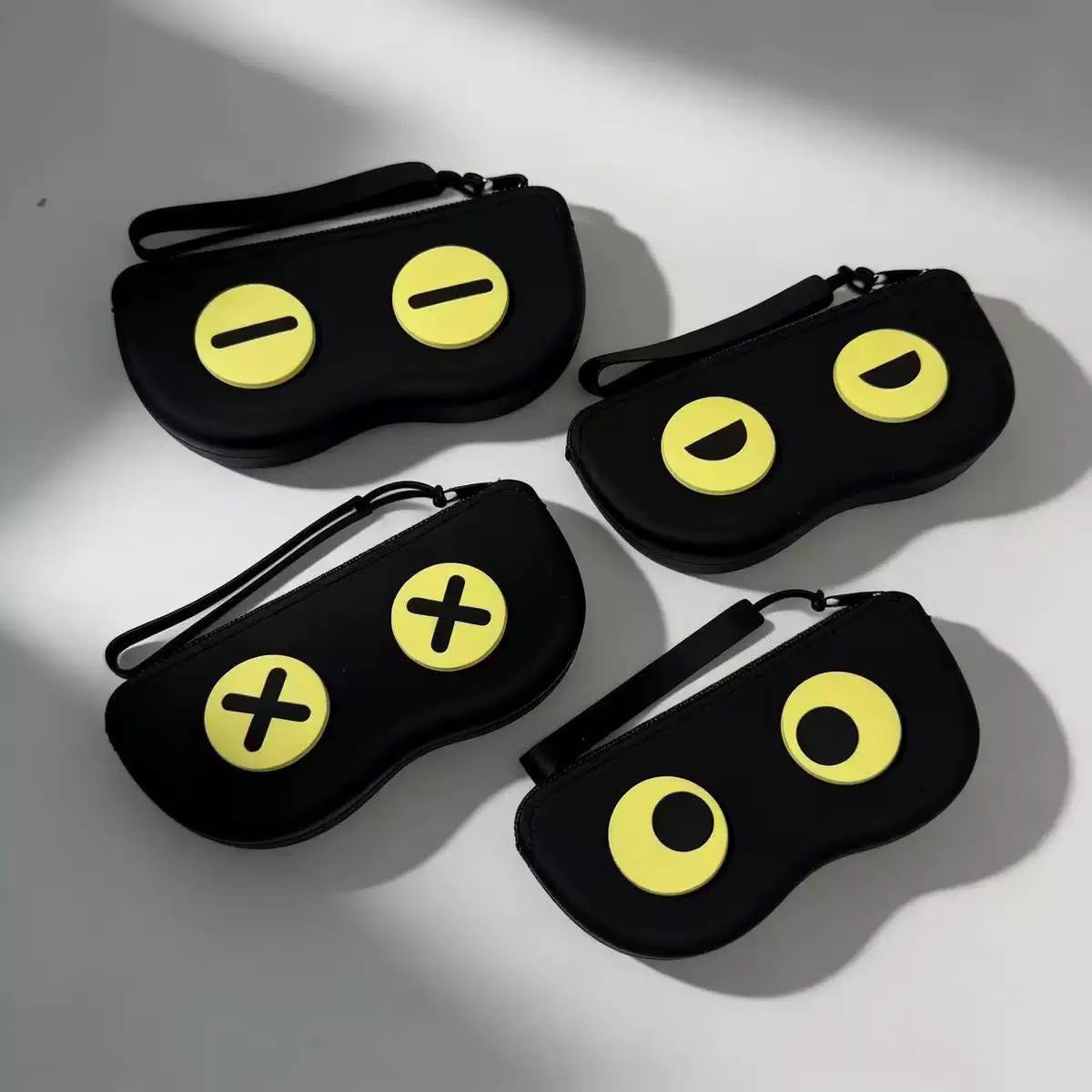 Four black protective phone cases with yellow cartoon eye details, arranged on a light gray surface with soft shadows.
